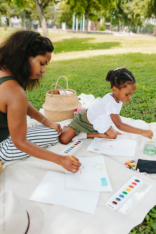 Mother and daughter painting together outdoors with paintbrushes and watercolors